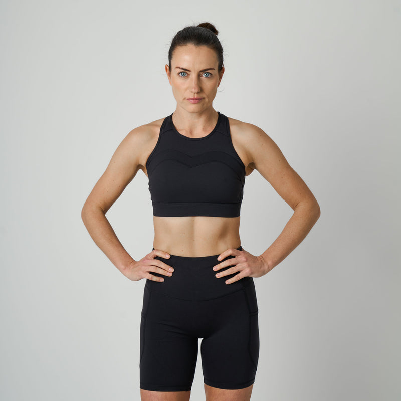 Woman wearing a black sports bra and shorts on a gray background