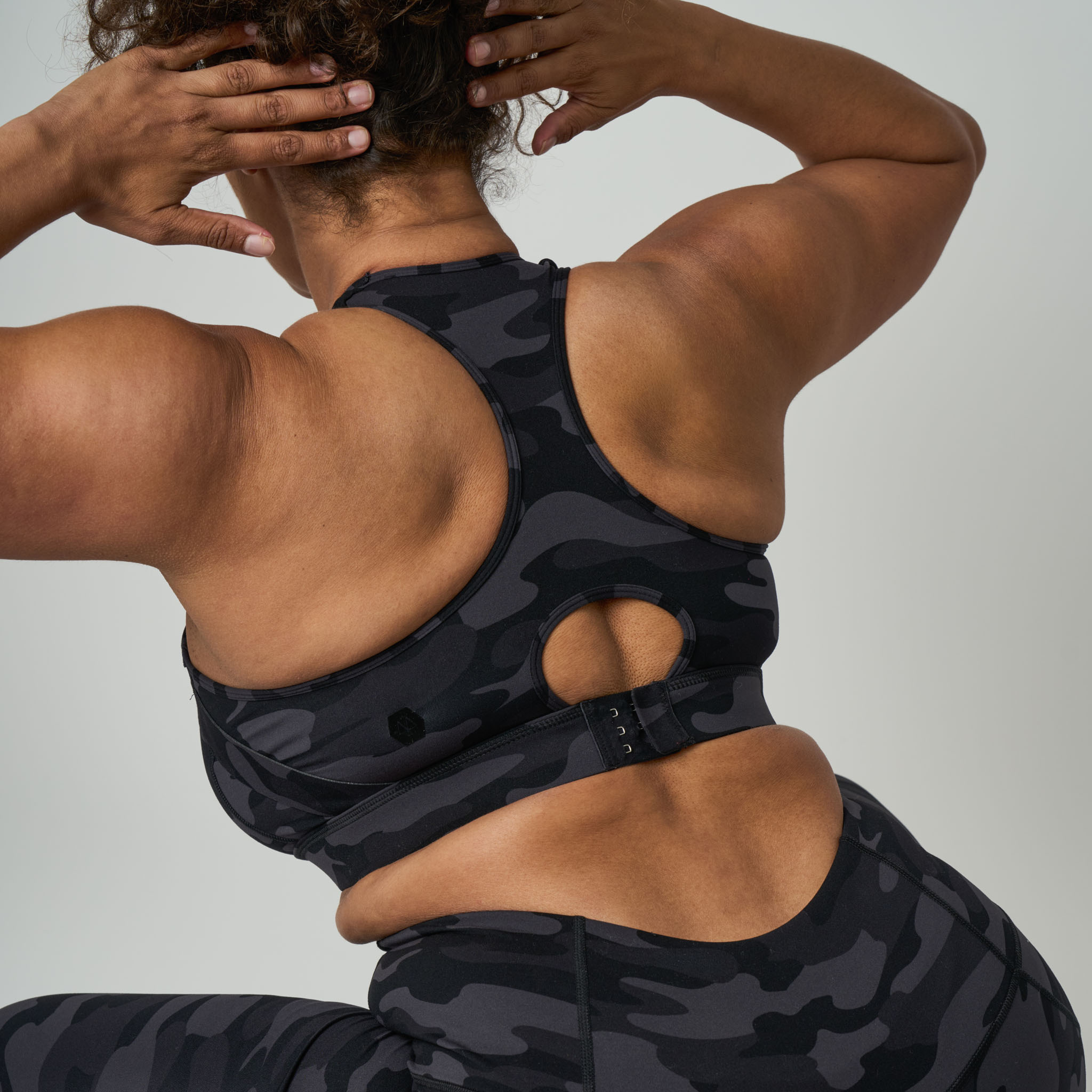 Person wearing a black camouflage sports bra and leggings on a light gray background