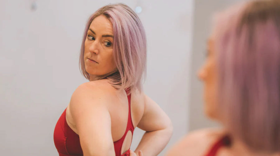 Blonde haired girl looking at her reflection in a mirror whilst looking to do her sports bra up