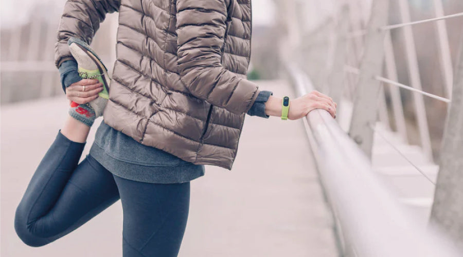 Woman dressed in winter running gear holding onto railing and stretching her hamstring