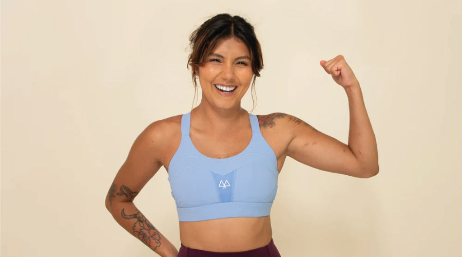 Gril flexing her bicep while smiling and wearing a cornflower blue Maaree Solidarity sports bra