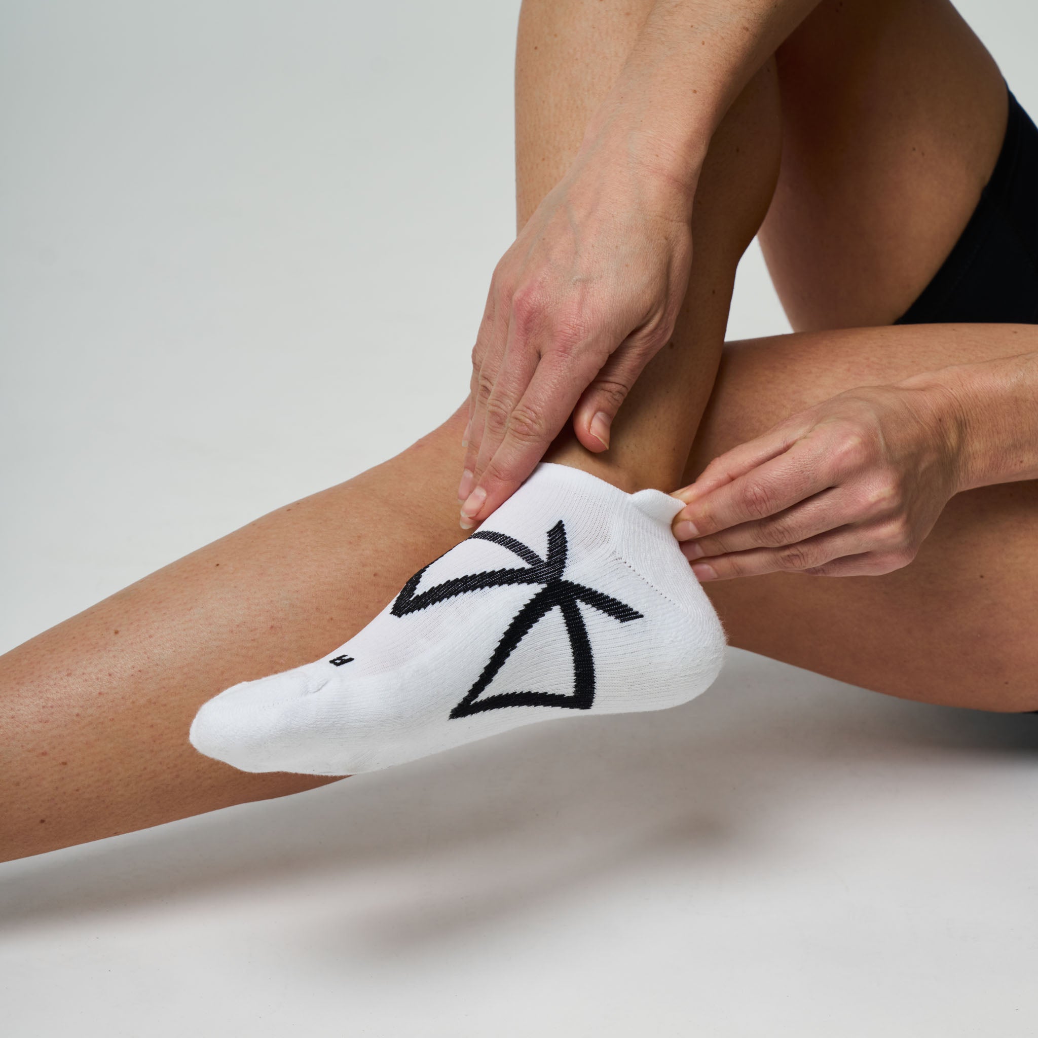 Person putting on a white ankle sock with black design on a neutral background