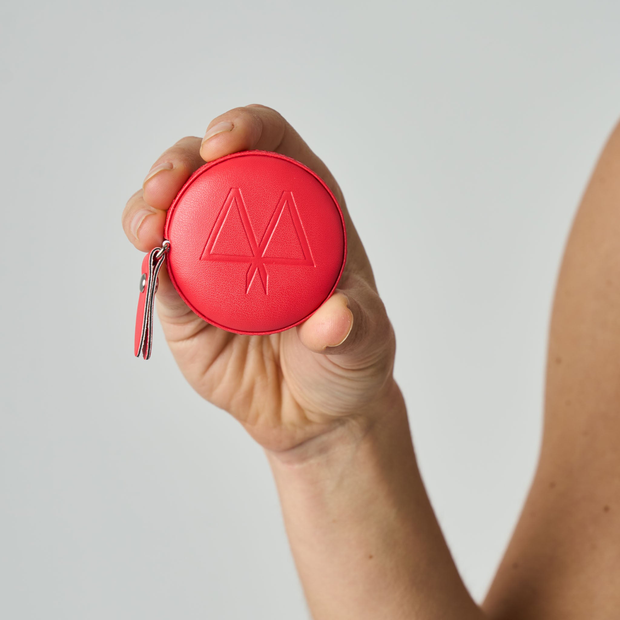 Hand holding a red tape measure with a logo against a light gray background