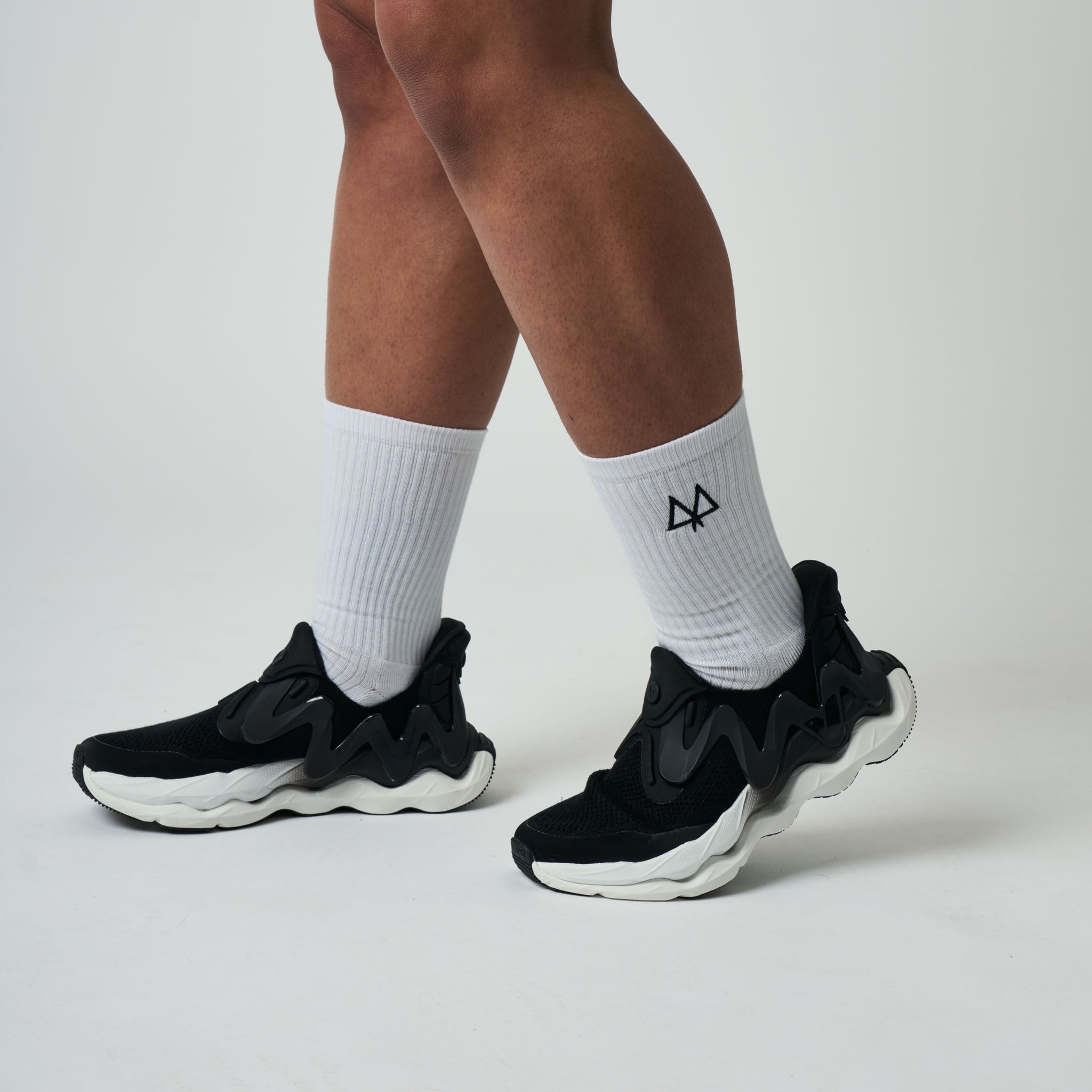 Black sneakers worn with white socks on a neutral background