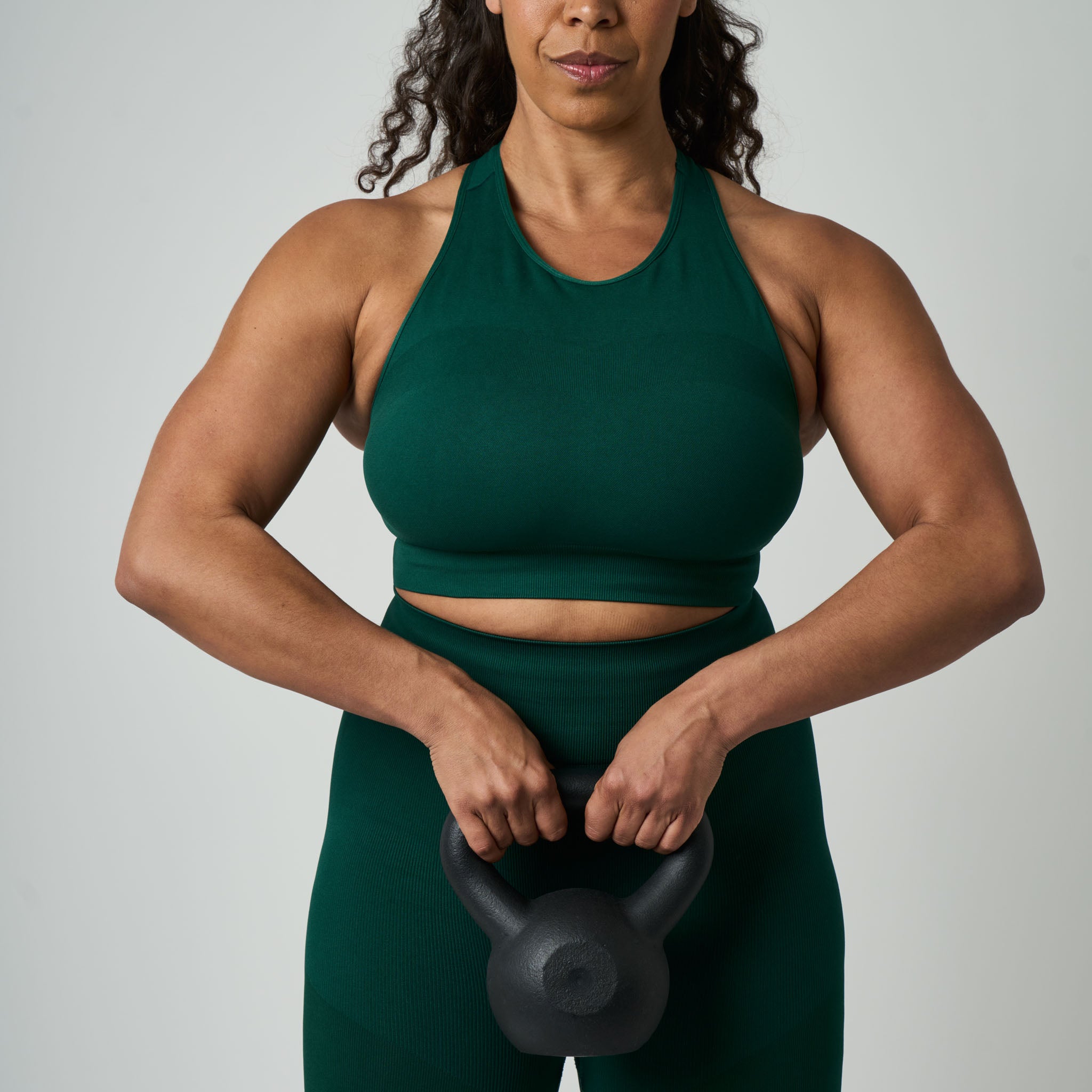 Woman in green athletic wear holding a black kettlebell against a plain background