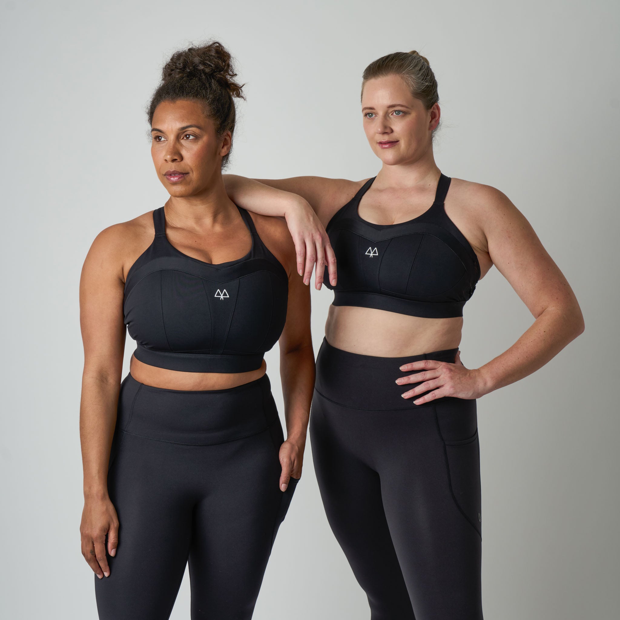 Two women wearing black athletic wear with a logo on a plain background