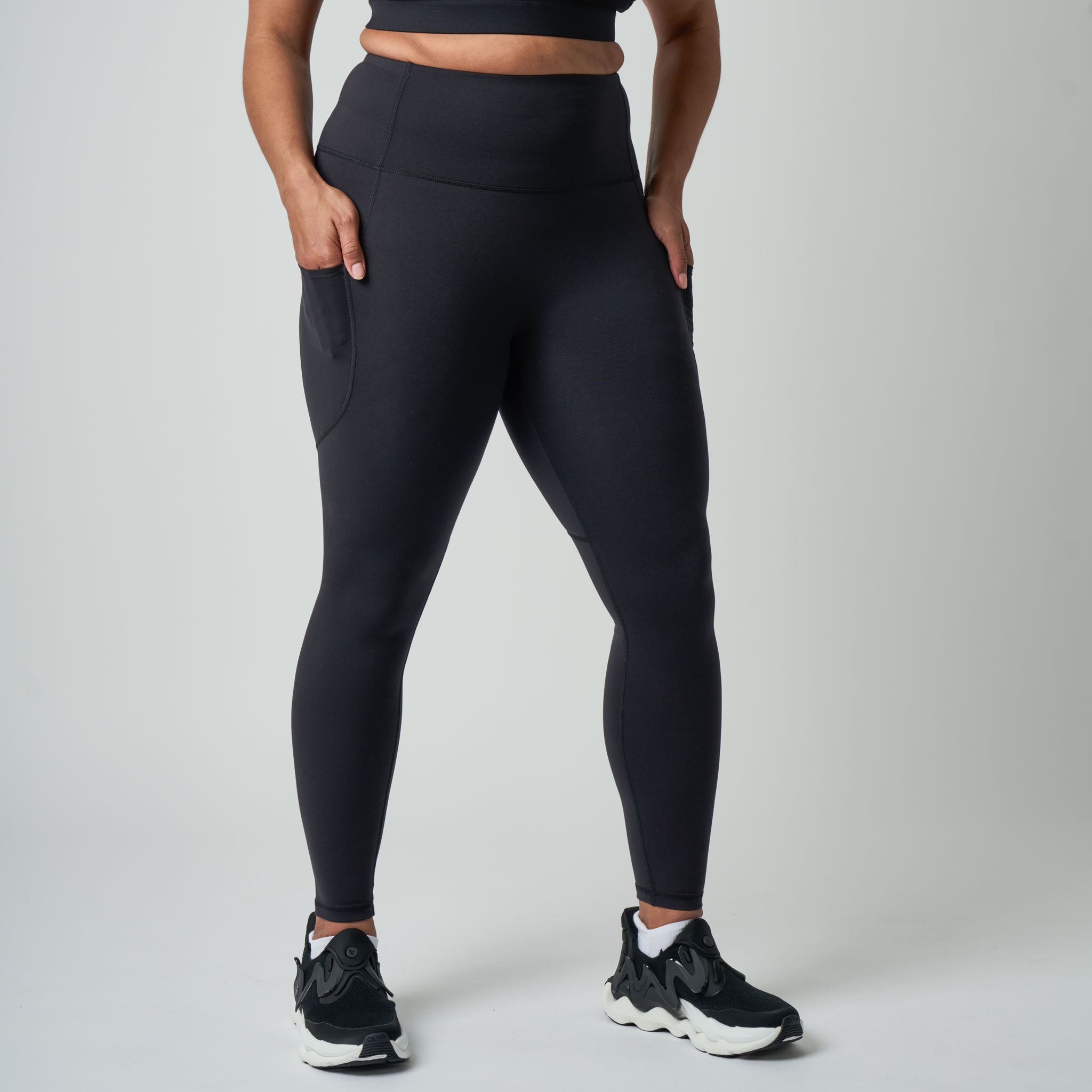 Person wearing black leggings and black sneakers on a light gray background