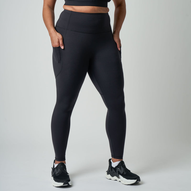Person wearing black leggings and black sneakers on a light gray background