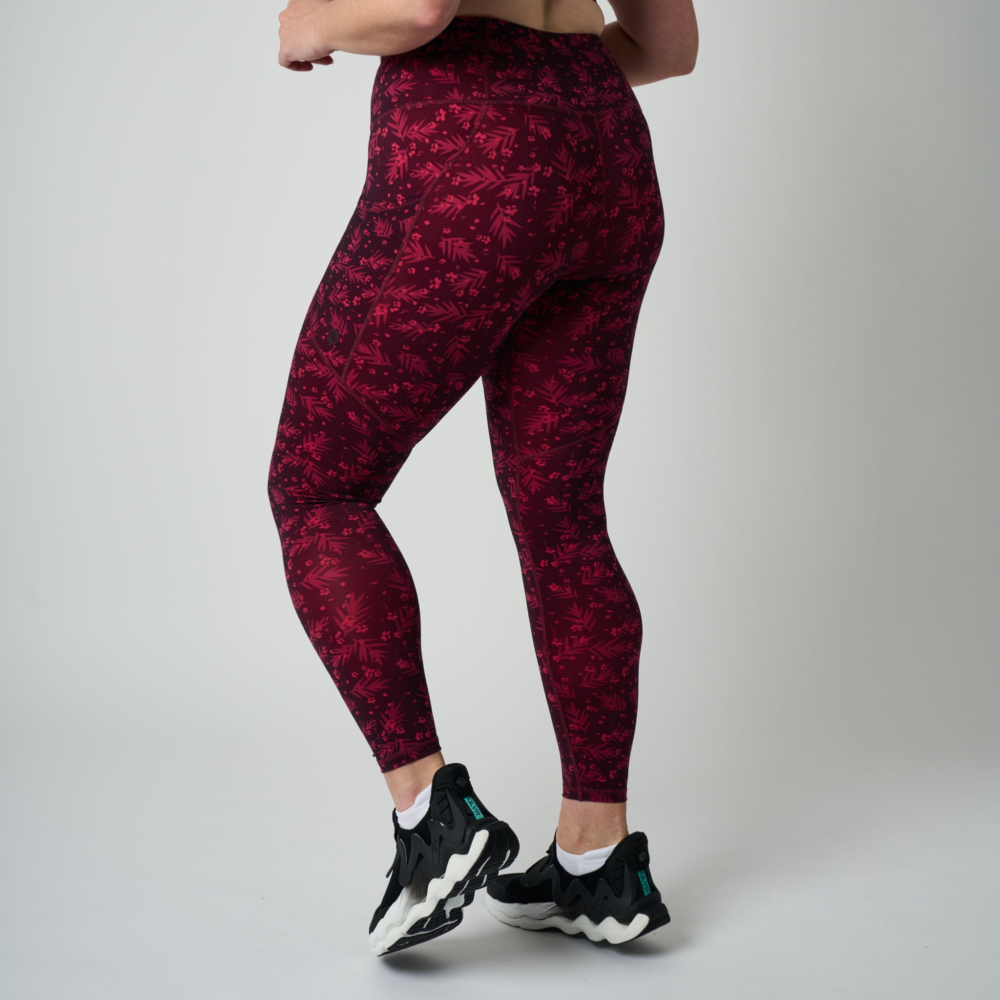 Person wearing red patterned leggings and black sneakers on a gray background