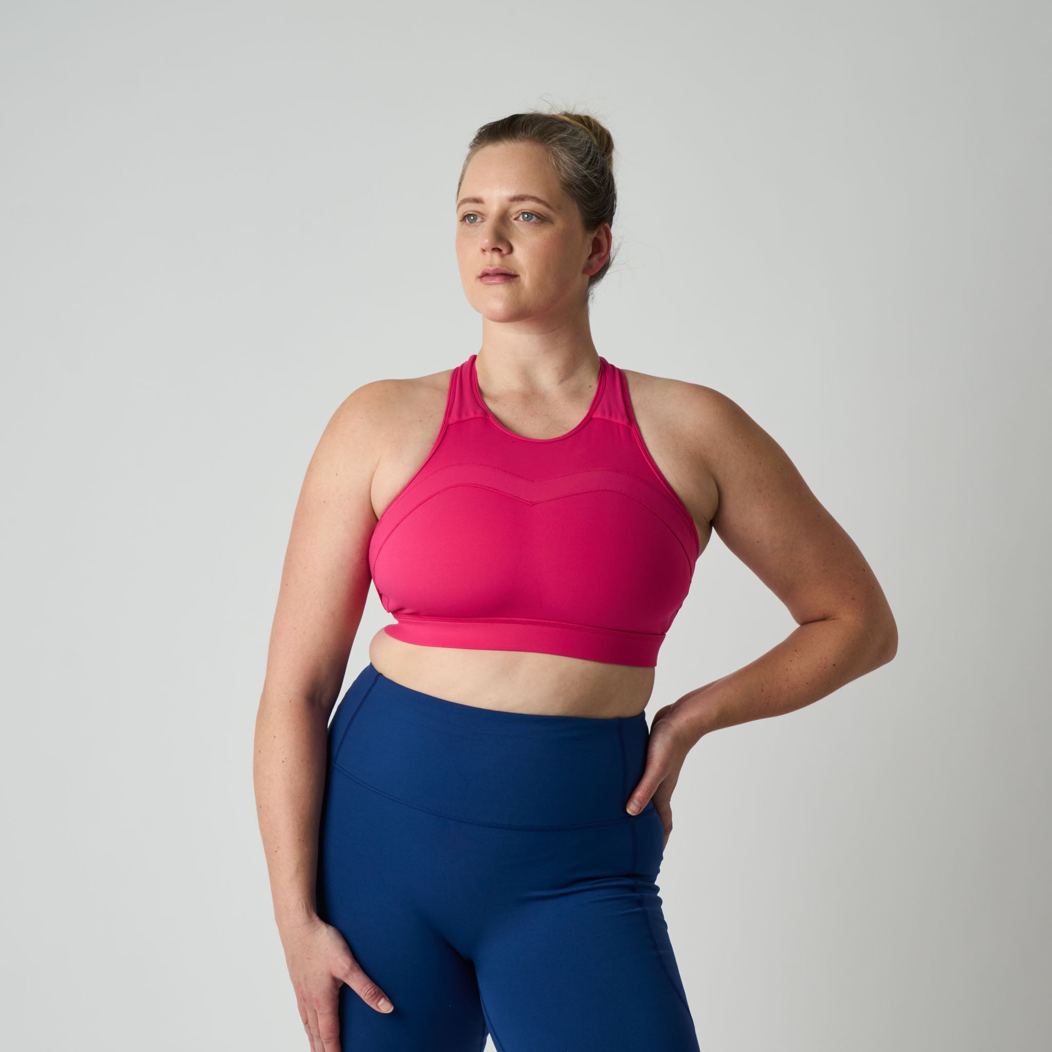 Woman wearing a pink sports bra and blue leggings on a gray background