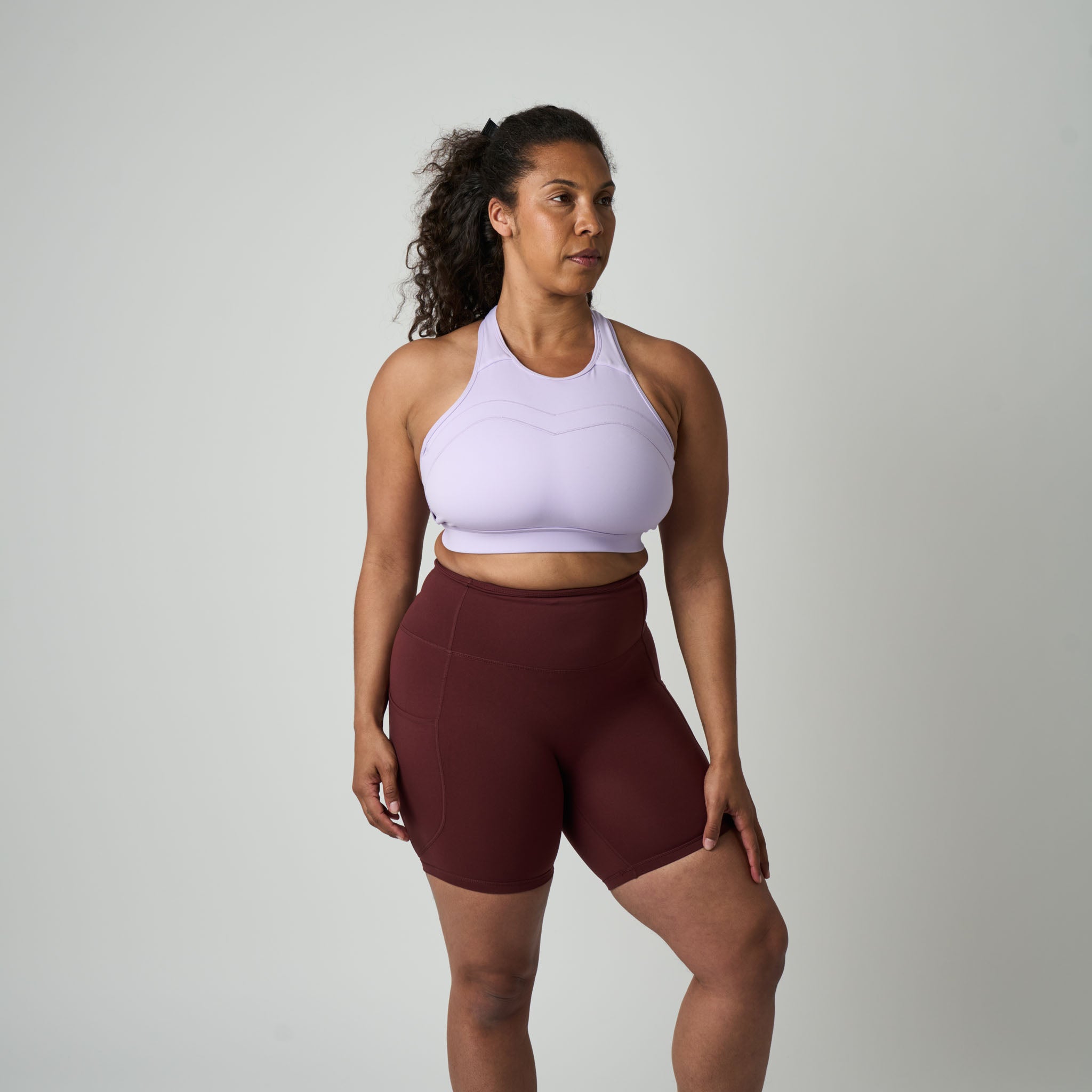 Woman wearing a white sports bra and maroon shorts on a gray background